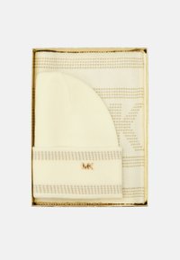 Set di berretto e sciarpa lavorati a maglia crema in una scatola dorata. La sciarpa presenta un motivo a strisce ripetuto e un logo sottile.