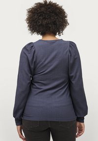Marineblå langærmet top med tekstureret stof, rund halsudskæring og puffede skuldre. Skræddersyet pasform fremhæver formen. Enkel bagsidedesign.