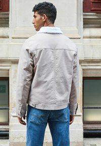 Lysegrå denimjakke med en faux shearling krave, der har en afslappet pasform, synlige sømme og knapdetaljer. Sæt den sammen med blå jeans.