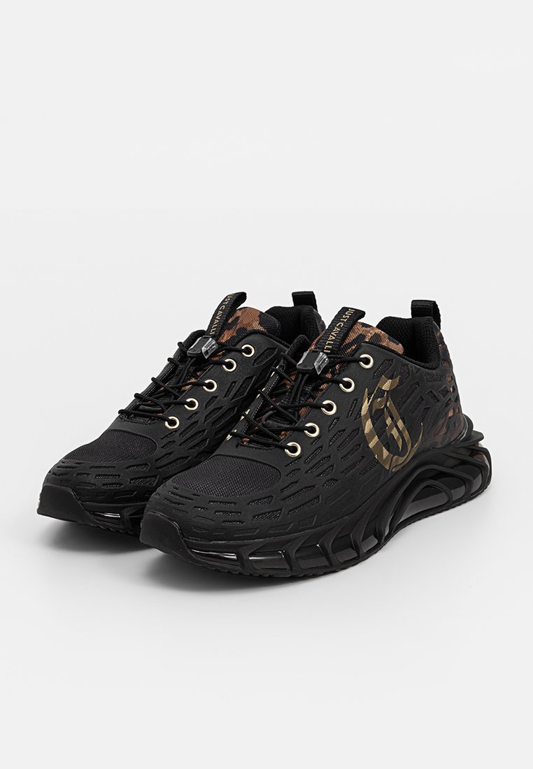 Schwarze Sportschuhe mit einem strukturierten Mesh-Obermaterial, goldenen Akzenten und einer einzigartigen Wellenmuster-Sohle. Mit Schnürsenkeln und einem gepolsterten Kragen.