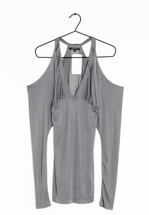 Vestido sin mangas gris con escote en V profundo y paneles de tela drapeada extendidos que cuelgan de los hombros, colgado en una percha negra.