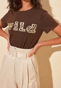 Brun bomullströja med ordet "WILD" i beige djurtryck. I kombination med högmidjade, krämfärgade byxor med bälte.