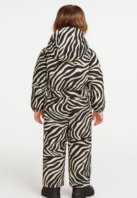 Zebra-print kindernieuwsuit in zwart en crèmekleur met een capuchon, elastische tailleband en zwarte laarzen. Heeft een gewatteerde structuur en lange mouwen.