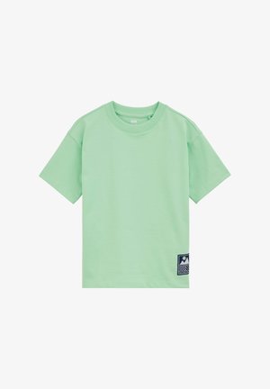 Camiseta de manga corta de color verde claro con cuello redondo y pequeño parche azul con iconos de montaña y ola en la parte inferior izquierda delantera.