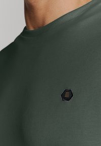 Groen crew-neck t-shirt gemaakt van gladde stof, met een klein zwart en goud hexagonaal logo op het linkerborstgebied.