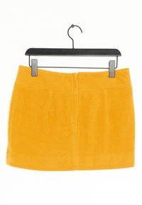 Kort gul kjol i mjukt tyg, med rak passform, två framfickor och dragkedja bak, hängande på en svart galge.