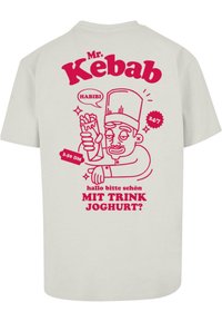 Hele beež t-särk, millel on detailne punane graafika karikatuuršefist, kes hoiab kebabit, koos mängulise fondiga teksti ja dekoratiivsete elementidega.