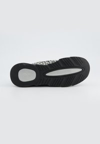 Semelle de chaussure de sport noire et grise avec un motif en caoutchouc texturé, présentant un logo circulaire et une conception de semelle intermédiaire durable.