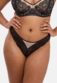 Ensemble de lingerie en dentelle noire comprenant un soutien-gorge à motifs floraux et un string assorti. Le tissu est transparent avec un bord noir contrastant et des détails en mesh.