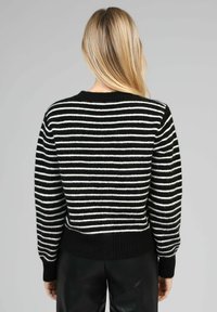 Pull en tricot rayé avec des couleurs noir et blanc, un col rond, un tissu texturé, des manches longues et un ourlet côtelé.