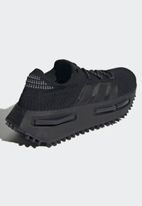 Black athletic shoe with a textured knit upper, prominent three-stripe logo, cushioned sole, and rubberized traction outsole.