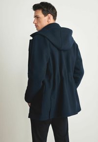 Granatowy płaszcz z kapturem o miękkiej fakturze. Posiada przednie kieszenie, dopasowaną talię oraz prosty krój, który sięga do długości bioder.