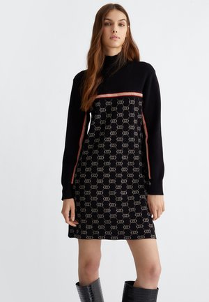 Abito lavorato a maglia con base nera, motivo a logo geometrico in beige, striscia orizzontale rossa sul petto e maniche lunghe.