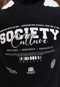 Черна суитшърт с бял надпис, съдържащ фрази като "Society Culture," и "Unfiltered Unbothered Unapologetic,", както и мотивиращо послание за самоизразяване.