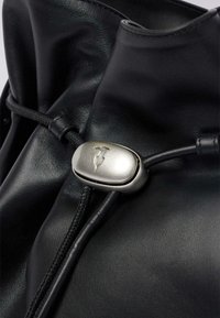 Borsa in pelle nera con chiusura a coulisse e toggle argentato. Texture liscia con lievi pieghe, che mettono in risalto i dettagli di design moderni.