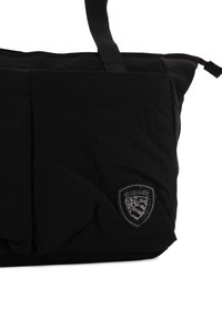 Sort nylon tote-bag med en tekstureret overflade, der har et fremtrædende logo-patch og to stofhåndtag til bæring.
