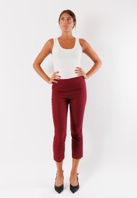 Top bianco senza maniche abbinato a pantaloni borgogna aderenti e cropped. Il modello indossa scarpe con tacco nere. Tessuto morbido, senza motivi visibili o accessori.