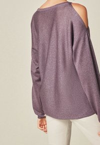 Purple glittery sweater with off-shoulder design, long sleeves, ribbed neckline, and textured fabric. Paired with light-colored pants.