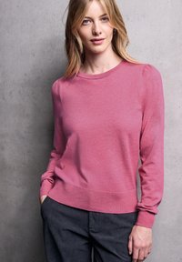 Helle rosa Langarm-Pullover mit rundem Ausschnitt und gerippten Bündchen, kombiniert mit dunkelgrauen Cordhosen. Weiche Textur und taillierter Schnitt.