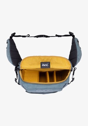 Borsa messenger blu e grigia con interno giallo, dotata di divisori imbottiti e spallacci in tessuto a rete per il comfort. Logo "evoc" visibile.