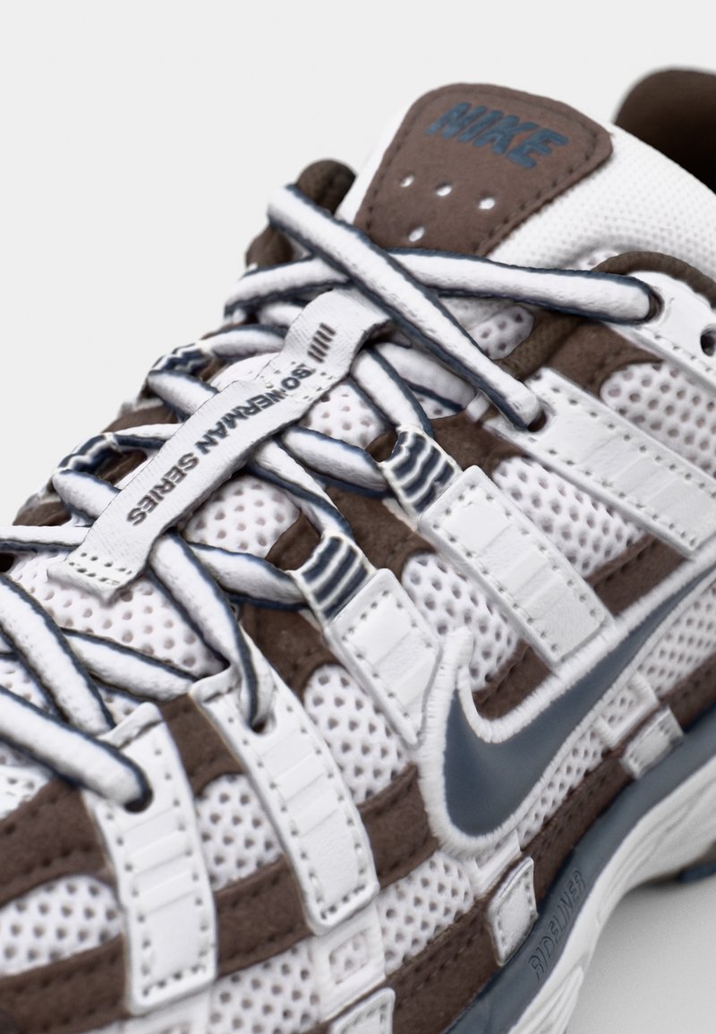 Witte en bruine Nike sneaker met mesh en suède materialen, uniek vetersysteem en een grijze swoosh logo.