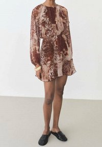 Robe mini florale dans des teintes rouges et brunes, avec des manches longues, des détails froncés et un tissu léger à la texture fluide.