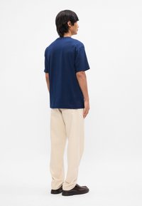 Ναυ blue βαμβακερό t-shirt με άνετη γραμμή, κοντό μανίκι και στρογγυλή λαιμόκοψη, φορεμένο με μπεζ παντελόνια και μαύρα παπούτσια.