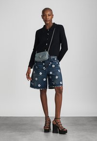 Fekete bordás hosszú ujjú felső, kék farmeranyagú, térd fölé érő sort fehér virágmintával hímzve, fém láncos válltáska, fekete platform sarkú cipő.