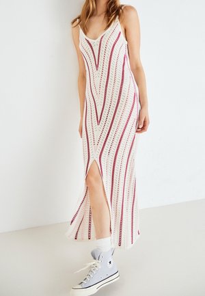 Robe maxi tricotée en crème avec des rayures zigzag roses. Elle présente de fines bretelles et une fente sur le côté, associée à des baskets montantes bleu clair.