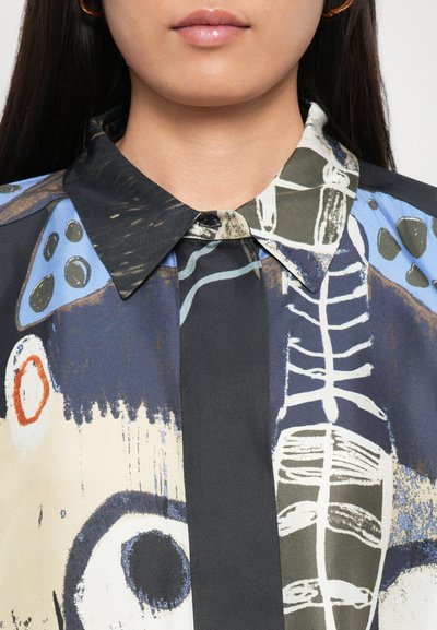 Patterned shirt featuring abstract designs in dark blue, beige, and green, with a pointed collar and button closure. Soft, textured fabric.
