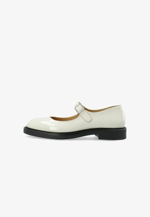 Weiße Lackleder-Mary-Jane-Schuhe mit runder Zehenpartie, flacher schwarzer Sohle und verstellbarem Riemen mit silberner Schnalle.