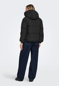 Musta toppatakki hupulla, suorakaiteen muotoisella tikillä ja joustavilla hihansuuilla. Yhdistetty korkeavyötäröisiin sinisiin farkkuihin.