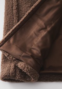 Veste en polaire marron avec un extérieur doux et texturé et une doublure en satin marron lisse. Dotée d'un col replié et d'un design superposé.
