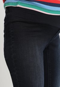 Donkerdenim jeans met een soepele textuur, voorzien van een slim fit ontwerp, en contrasterend met een meerkleurige gestreepte top ter hoogte van de taille.