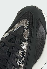 Čierne športové topánky s textúrovanou sieťovinou a hadovým vzorom v šedej a striebornej farbe. Čierne šnúrky a hladká gumová podrážka.