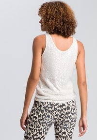 Débardeur blanc sans manches orné de sequins avec un dos en arrondi, associé à un pantalon ajusté beige et noir à motifs présentant un design géométrique unique.