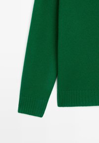 Grüner, gestrickter Pulloverärmel mit geripptem Bündchen und Saum auf einem weißen Hintergrund, der Textur und Stoffdetails zeigt.