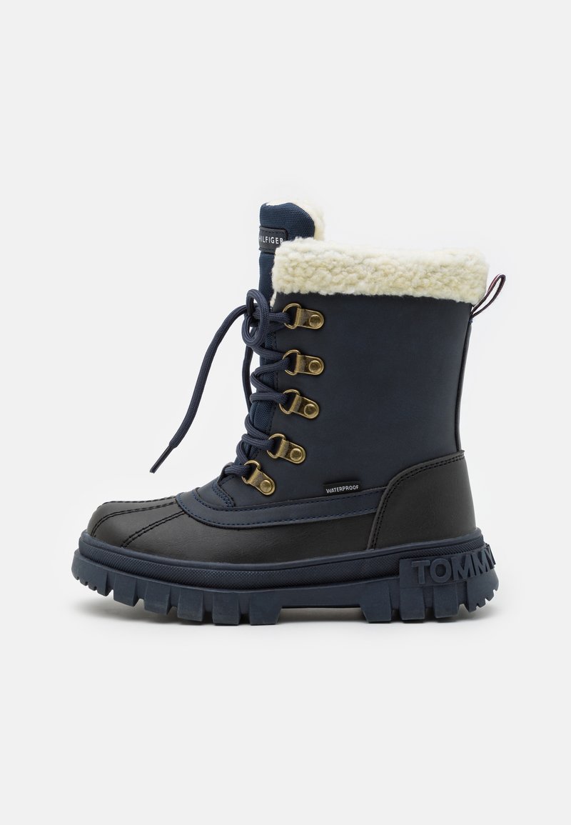 Botte d'hiver imperméable bleu marine avec semelle épaisse en caoutchouc, fermeture à lacets devant, œillets métalliques et doublure en polaire blanche en haut.