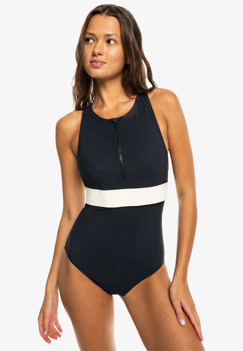 Musta uimapuku, jossa on korkea kaula-aukko, etuvetoketju ja kontrastoiva valkoinen vyökohtana. Valmistettu sileästä, joustavasta materiaalista.