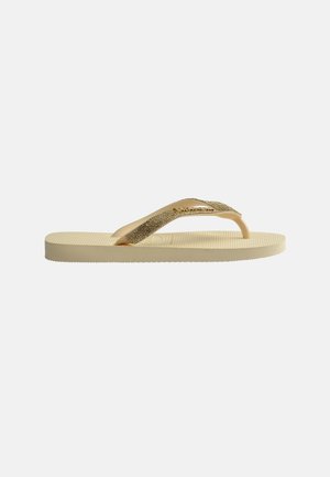 Tongs beiges avec semelle texturée et brides dorées scintillantes, vues de profil sur un fond clair.