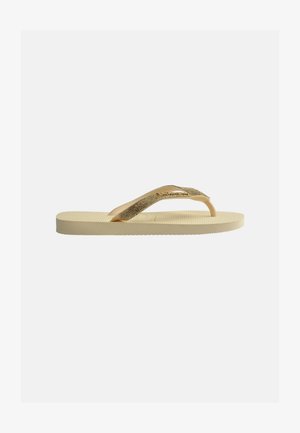 Beige flip-flop-sandal med teksturert såle og glitrende gullstropper, vist fra siden på en lys bakgrunn.