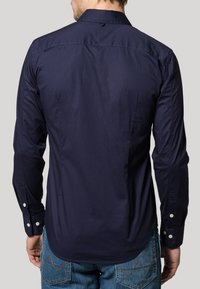 Navy long-sleeve shirt with button cuffs, fitted design, smooth texture, and back yoke detail, seen from the rear against a neutral background.