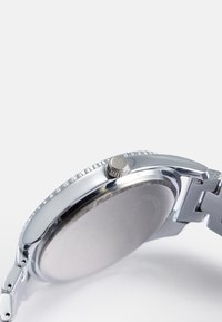 Orologio argento con cassa rotonda in acciaio inossidabile, ghiera texturizzata e corona a pressione. Il cinturino è composto da maglie, che ne migliorano la resistenza.