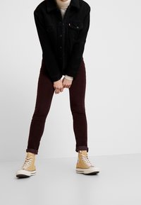 Chaqueta de mezclilla negra con un cuello texturizado, combinada con jeans skinny burdeos y zapatillas altas color topo.
