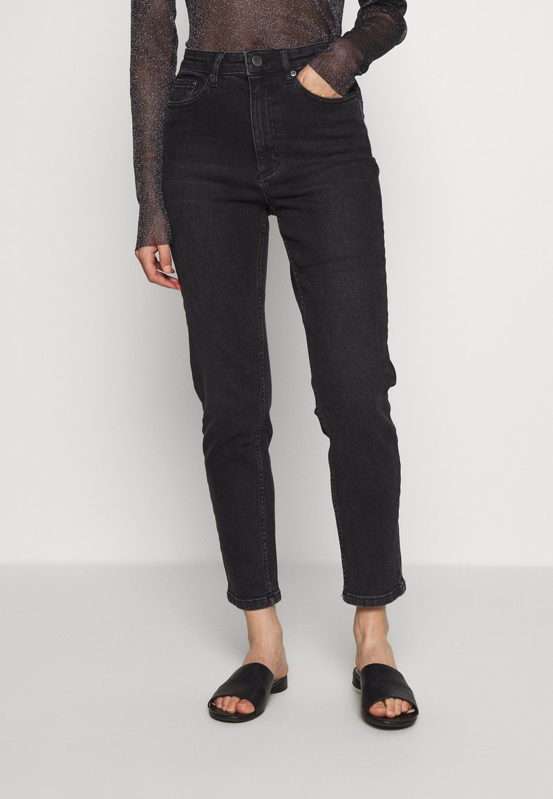 Jean noir taille haute à coupe slim, chevilles effilées et design classique à cinq poches, assorti à des sandales noires à enfiler.