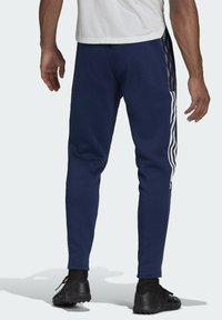 Navy athletic pants made of soft fabric, featuring white side stripes, tapered legs, and an elastic waistband for a comfortable fit.