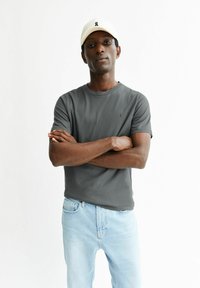 Graues Baumwoll-T-Shirt mit kurzen Ärmeln und rundem Ausschnitt, kombiniert mit hellblauen Jeans. Ein weißes Cap mit Logo vervollständigt das Outfit.