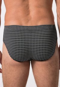 Slip da bagno neri con un motivo circolare bianco ripetuto, realizzati in tessuto liscio e con un taglio a vita bassa.