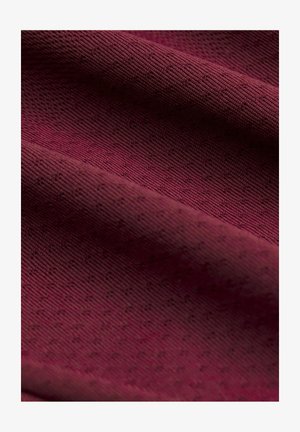 Tissu rouge profond avec un motif tricoté texturé, délicatement plié pour montrer un fin côtelé doux et des points légèrement en relief sur toute la surface.