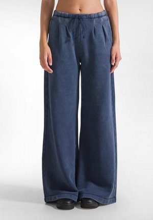 Pantaloni della tuta a gamba larga color navy, realizzati in tessuto morbido con vita regolabile tramite cordoncino, presentano una vestibilità comodamente ampia e dettagli plissettati nella parte anteriore.